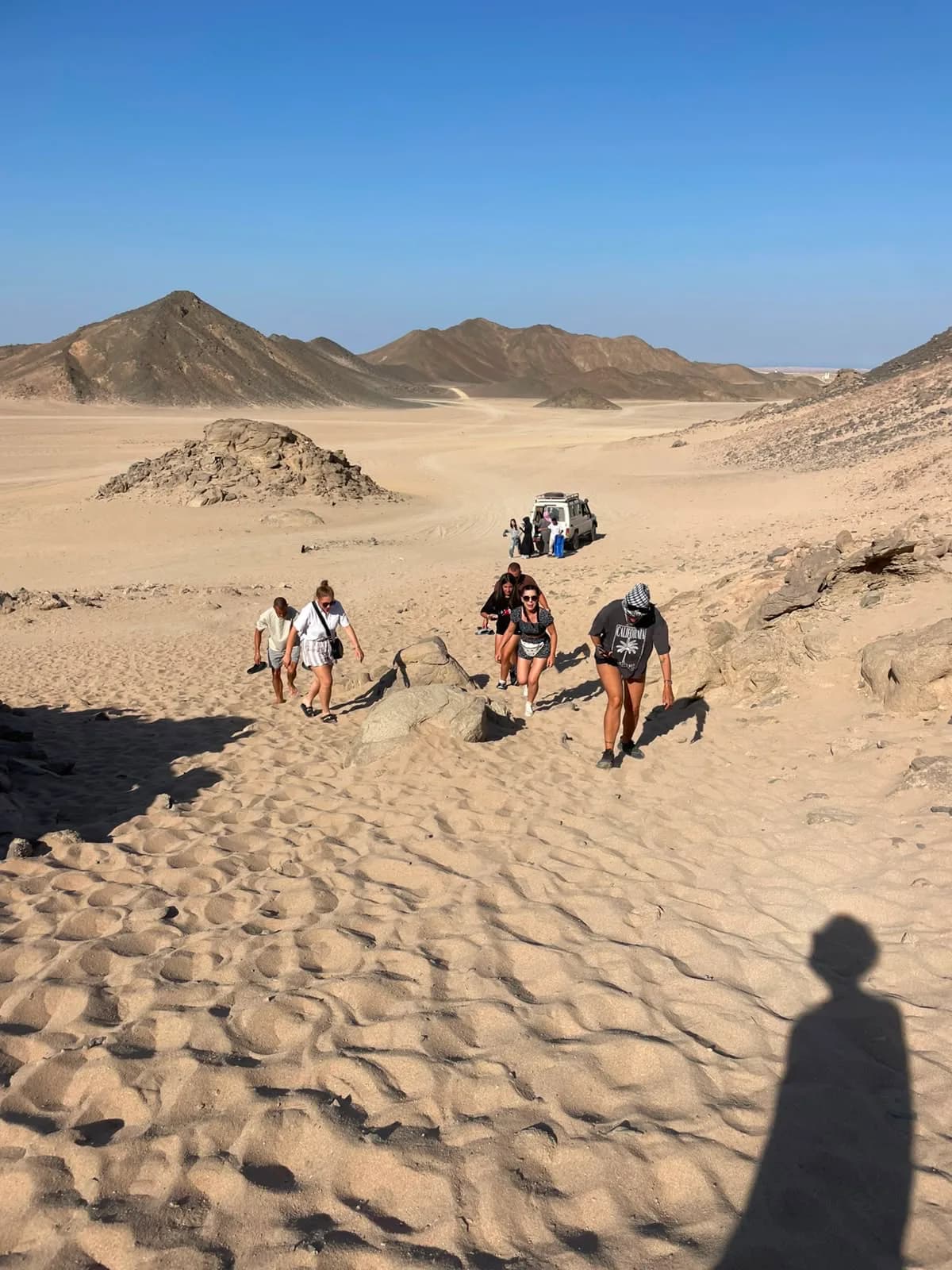 Tourists walking through the desert dunes near a Jeep