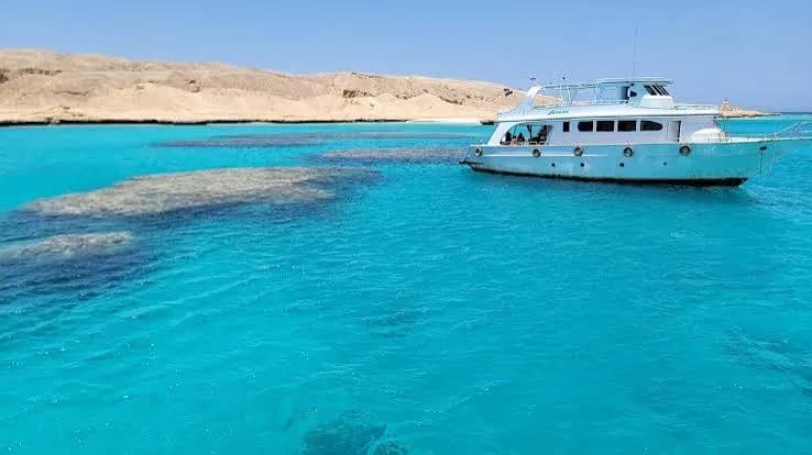 Dive boat anchored over a shallow turquoise reef near desert cliffs