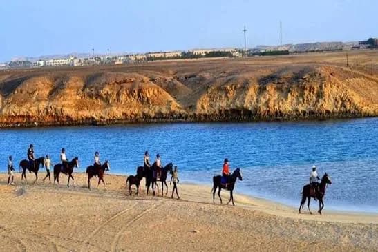Line of riders on horseback beside a desert lagoon