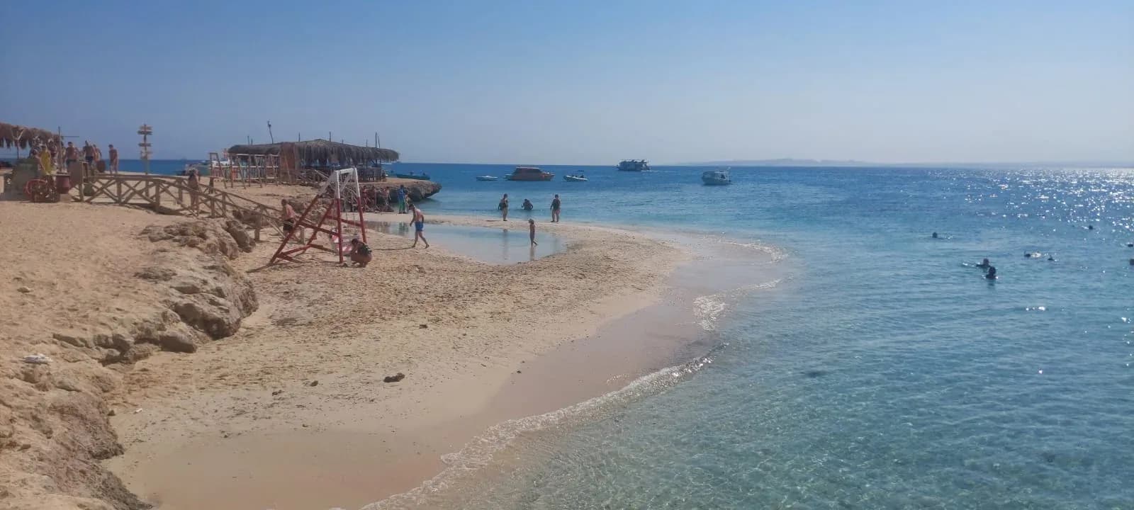 Beach and turquoise water at Magawish Island with swimmers and boats