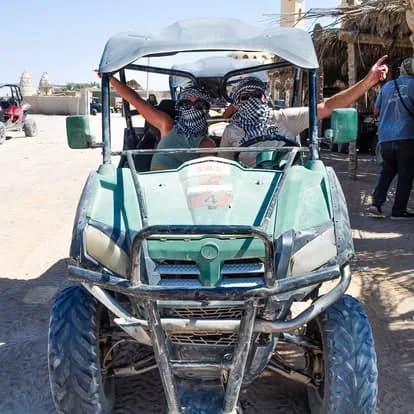 Two guests in desert scarves riding a buggy through the Bedouin village