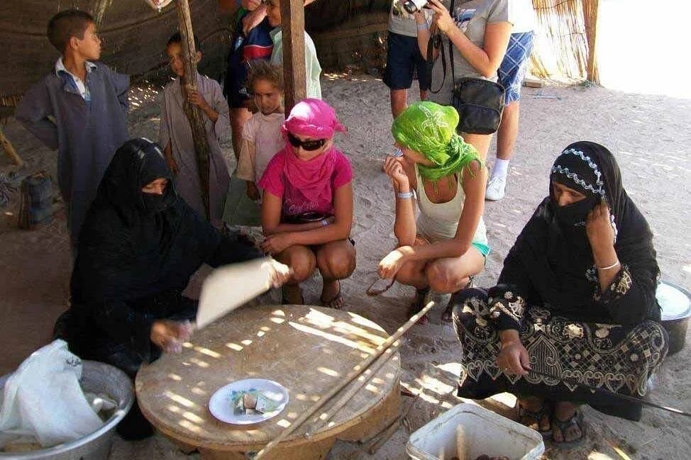 Bedouin women preparing bread with visiting children watching
