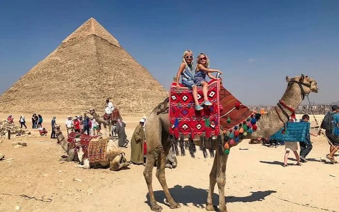 Tourists riding camels in front of the Pyramids of Giza