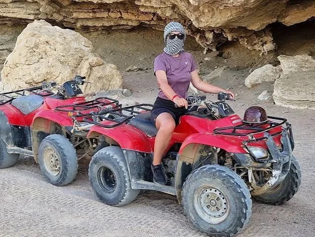Guest sitting on a red quad bike beside desert rock formations
