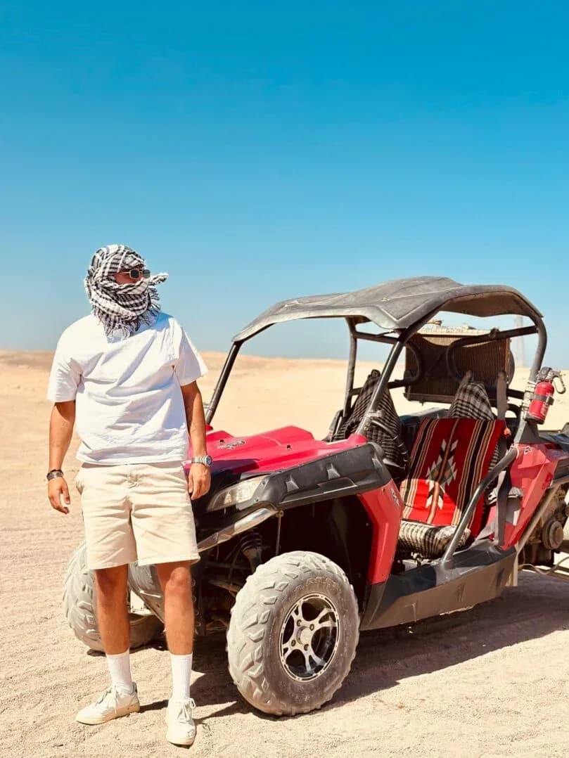Guest wearing a traditional scarf standing beside a red buggy before the desert ride