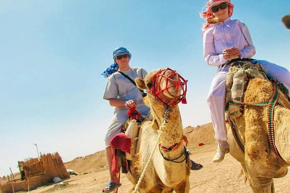 Camel riders with a Bedouin village hut in the background