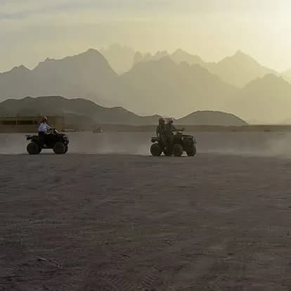 Two quad bikes riding across open desert with mountains silhouetted in the background