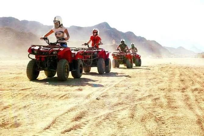 Convoy of quad bikes riding through the desert with mountains behind