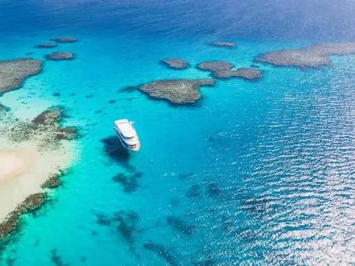 Aerial view of a boat anchored beside coral reefs and a sandy island near Hamata