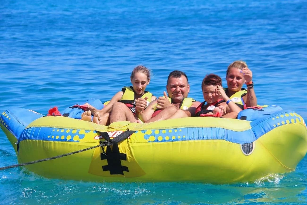 A family of four laughing together on an inflatable water tube being towed across the Red Sea
