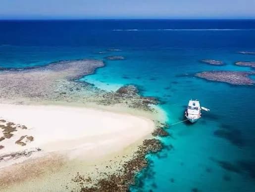 Aerial view of a boat moored beside a white sand spit surrounded by turquoise reef