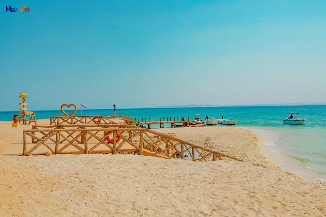 Wooden footbridge and heart sculpture on the beach at Magawish Island with boats offshore
