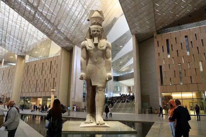 Statue of Ramesses II standing in the Grand Egyptian Museum's main atrium, with visitors below