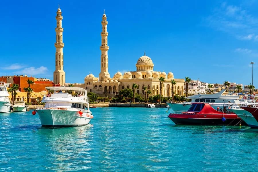 The El Mina Mosque and marina waterfront in Hurghada under a bright blue sky, with excursion boats moored in the foreground